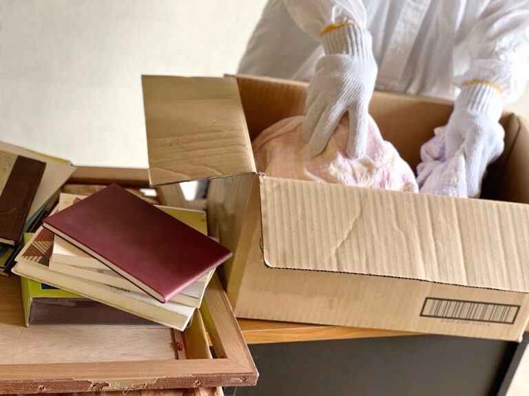 Hands wearing gloves putting clothes into a cardboard box
